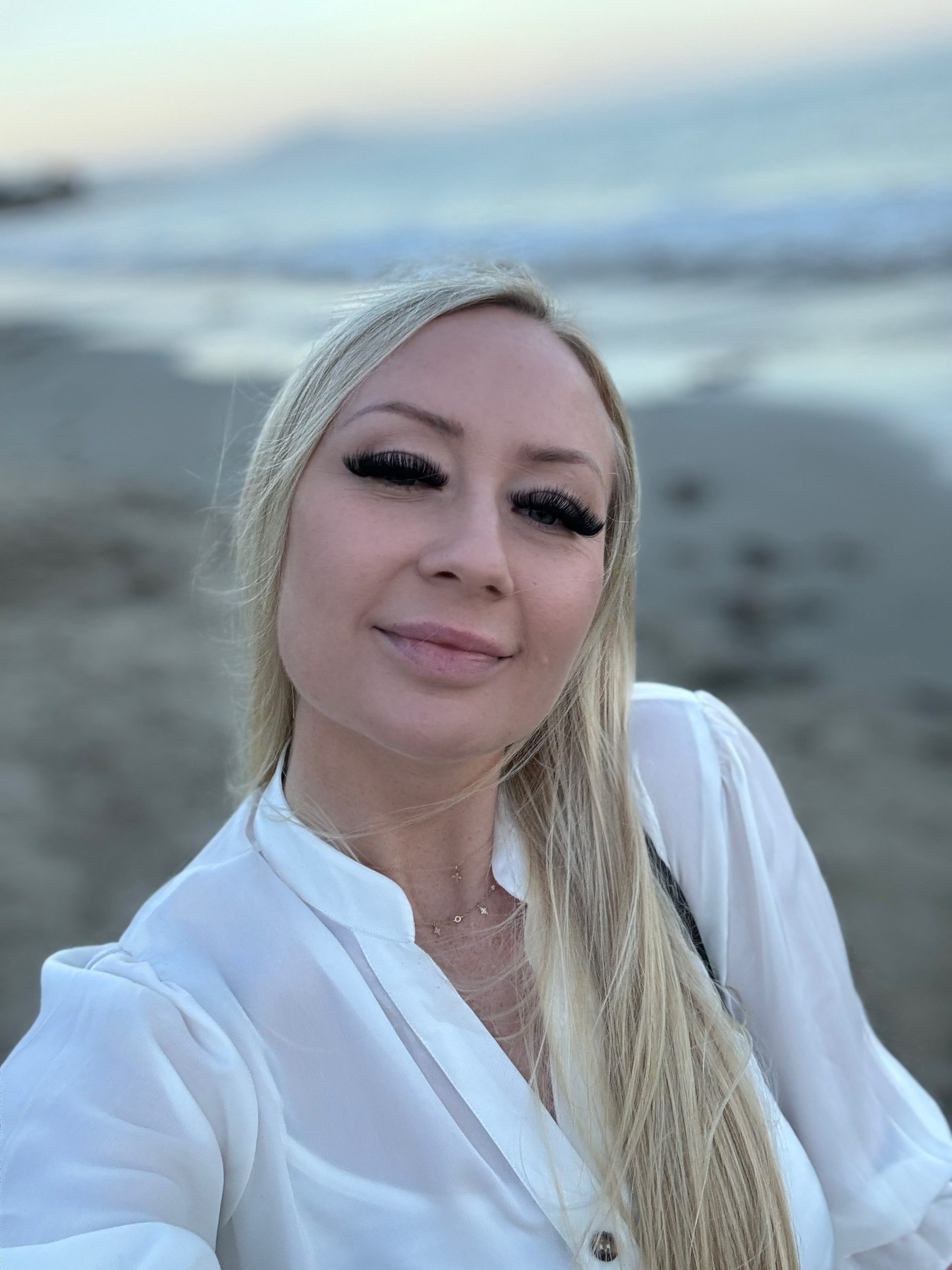 A woman with long blonde hair standing on the beach.