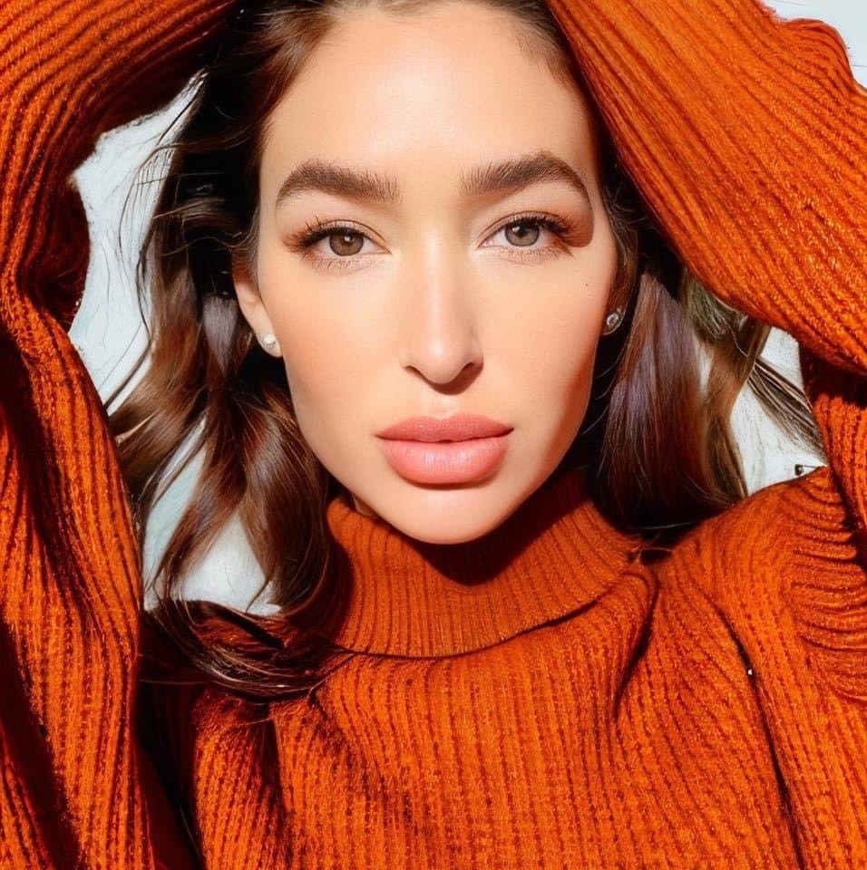 A woman in an orange sweater posing for the camera.