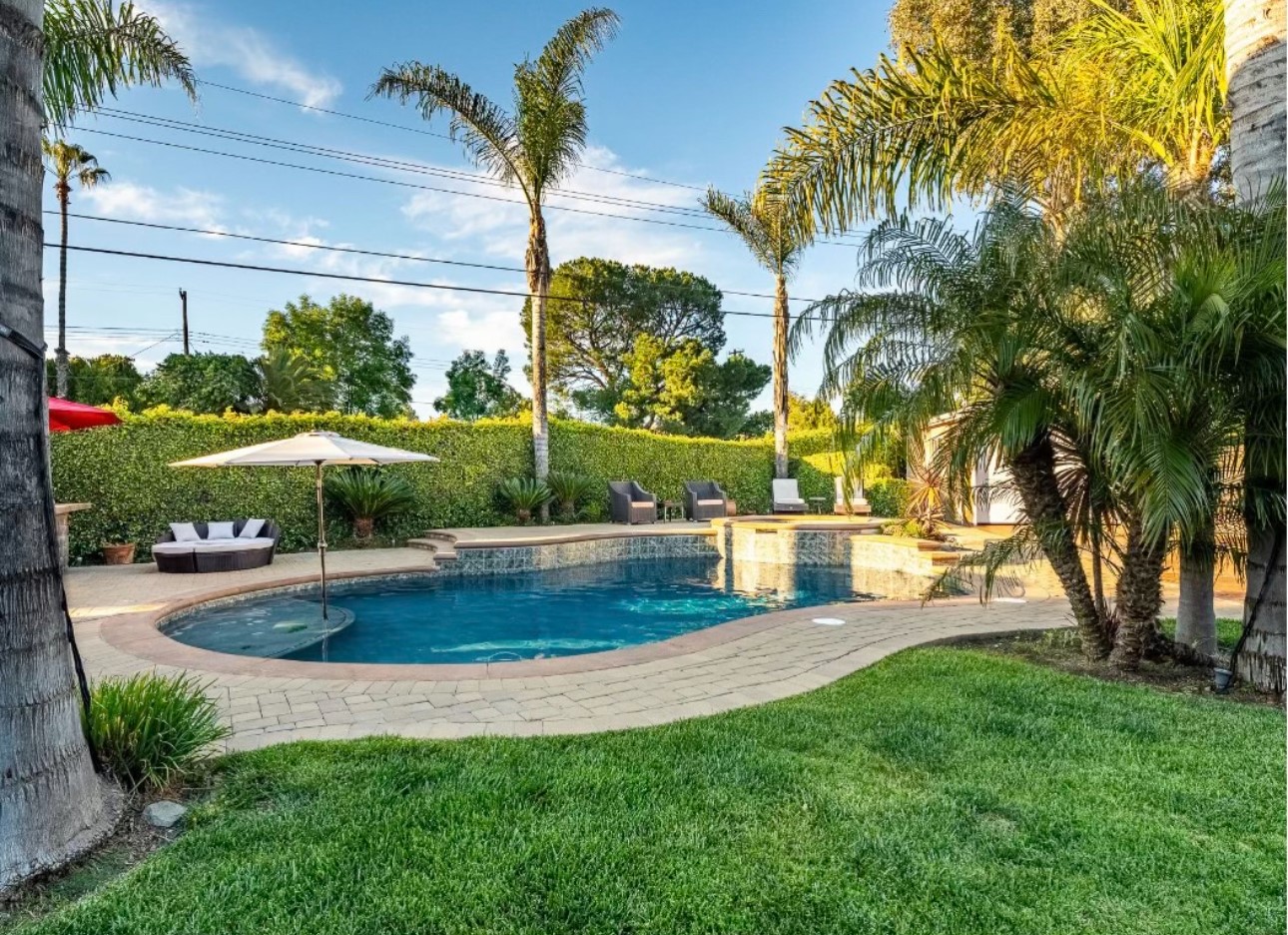 A pool with an umbrella and chairs in the back yard.