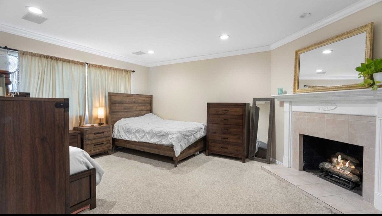 A bedroom with a bed, dresser and fireplace.