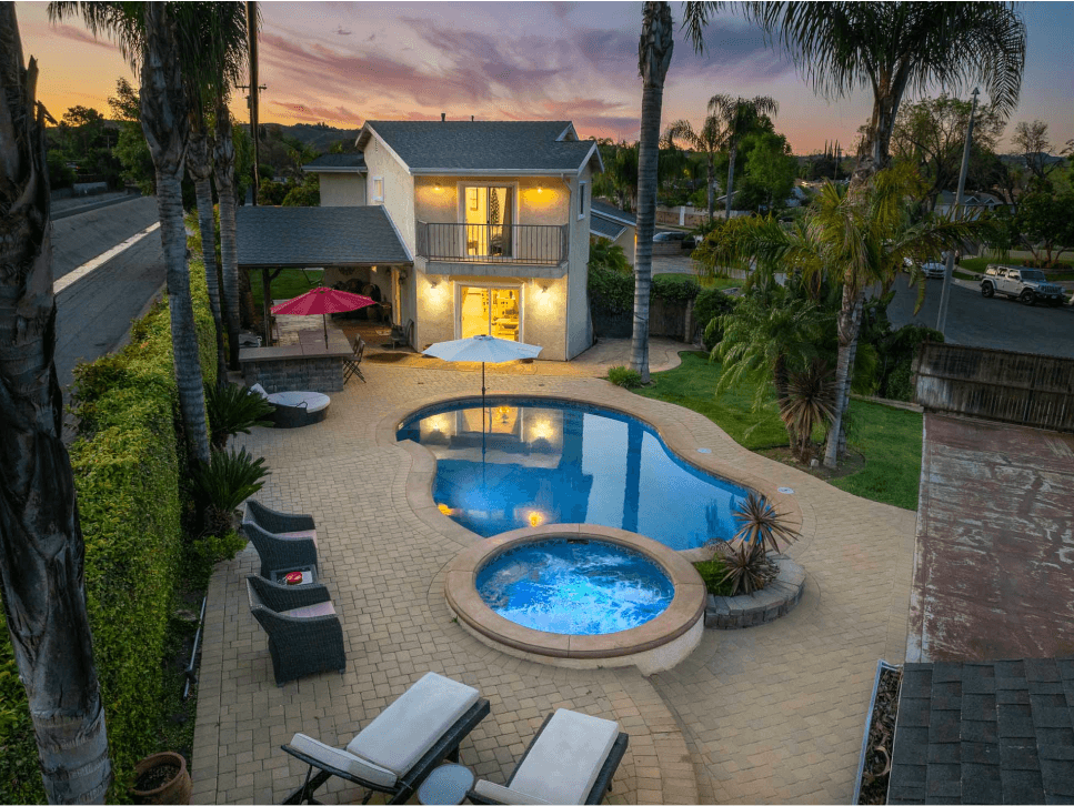 A backyard with pool and hot tub at dusk.